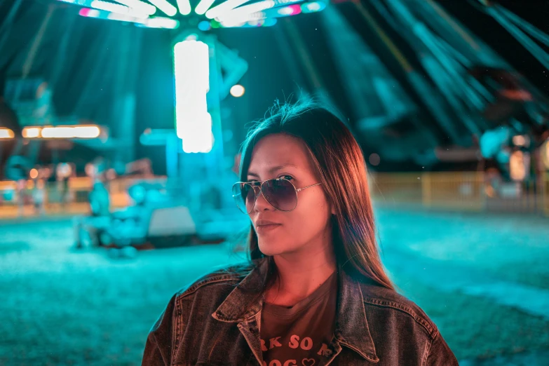 a woman standing in front of a carnival ride at night, a portrait, by Julia Pishtar, pexels contest winner, girl wearing round glasses, slightly tanned, woman in streetwear, avatar image