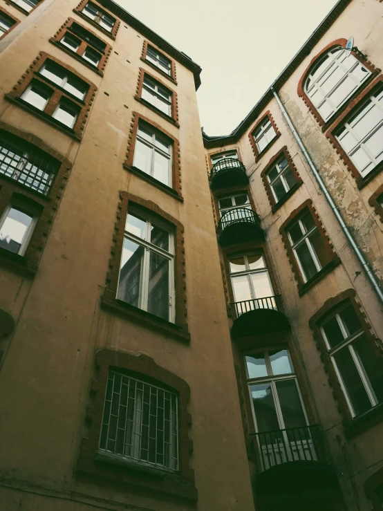 a tall building with lots of windows and balconies, a photo, inspired by Albert Paris Gütersloh, pexels contest winner, art nouveau, an abandonded courtyard, muted colors. ue 5, narrow and winding cozy streets, hannover