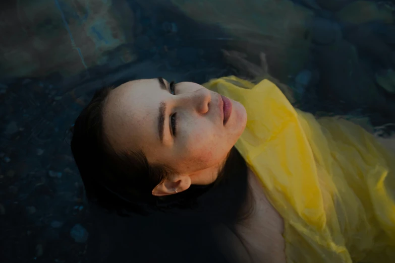 a woman floating in a body of water, with yellow cloths, thoughtful, lit from the side, portait image