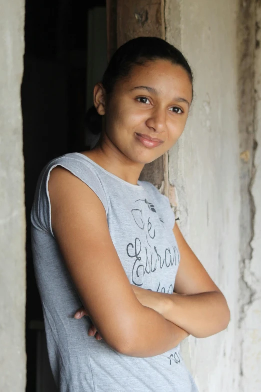 a woman standing in a doorway with her arms crossed, inspired by Gina Pellón, happening, around 1 9 years old, light-brown skin, colombian, lovingly looking at camera