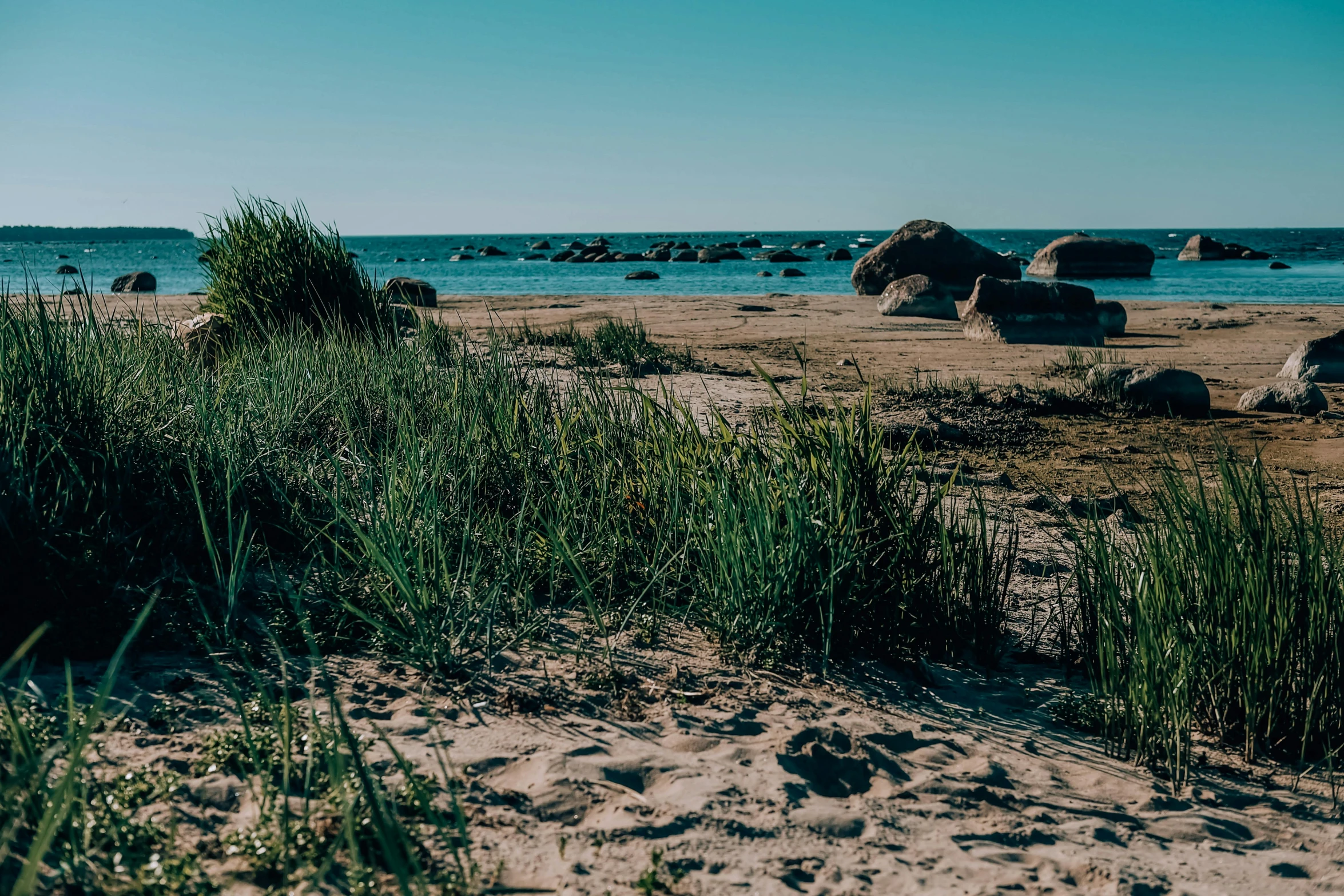 a couple of rocks sitting on top of a sandy beach, a picture, unsplash, hurufiyya, rocky grass field, inlets, victorian arcs of sand, campsites