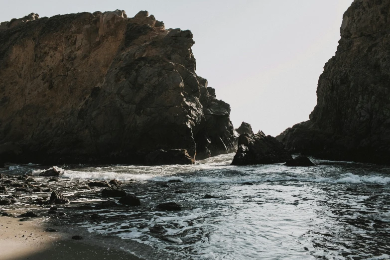 a couple of rocks sitting on top of a sandy beach, in the water, pch, background image, unsplash photography