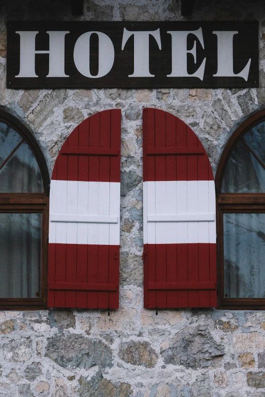 a hotel sign on the side of a building, inspired by Wes Anderson, unsplash, tall arched stone doorways, red and white stripes, alpine architecture, shutters