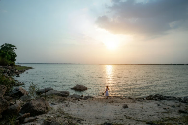 a couple of people standing on top of a sandy beach, during a sunset, sitting in front of a lake, sri lankan landscape, journalism photo