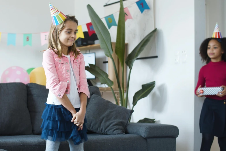 two little girls standing next to each other in a living room, pexels contest winner, happening, wearing a party hat, wearing jacket and skirt, teenager girl, tiny girl looking on