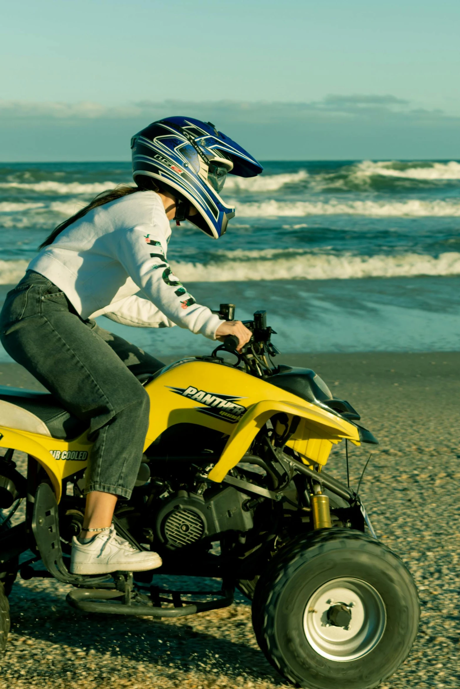 a woman riding a yellow atv on top of a sandy beach, motorcycle helmet, oceanside, detailing, teen