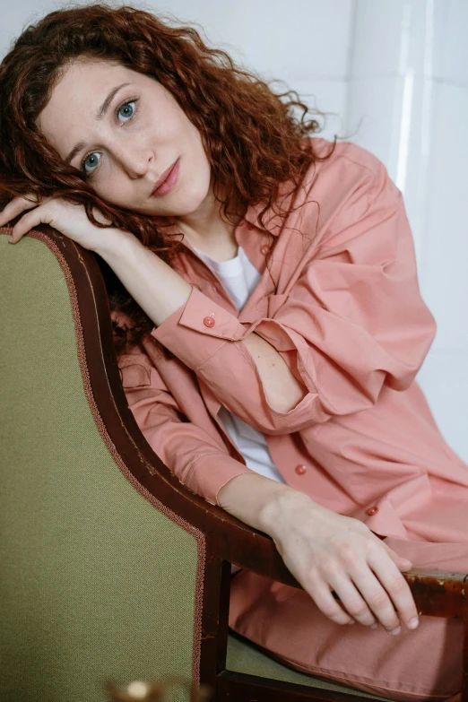 a woman sitting on top of a wooden chair, inspired by Anita Malfatti, trending on pexels, renaissance, pink shirt, ( redhead, curly, wearing jacket