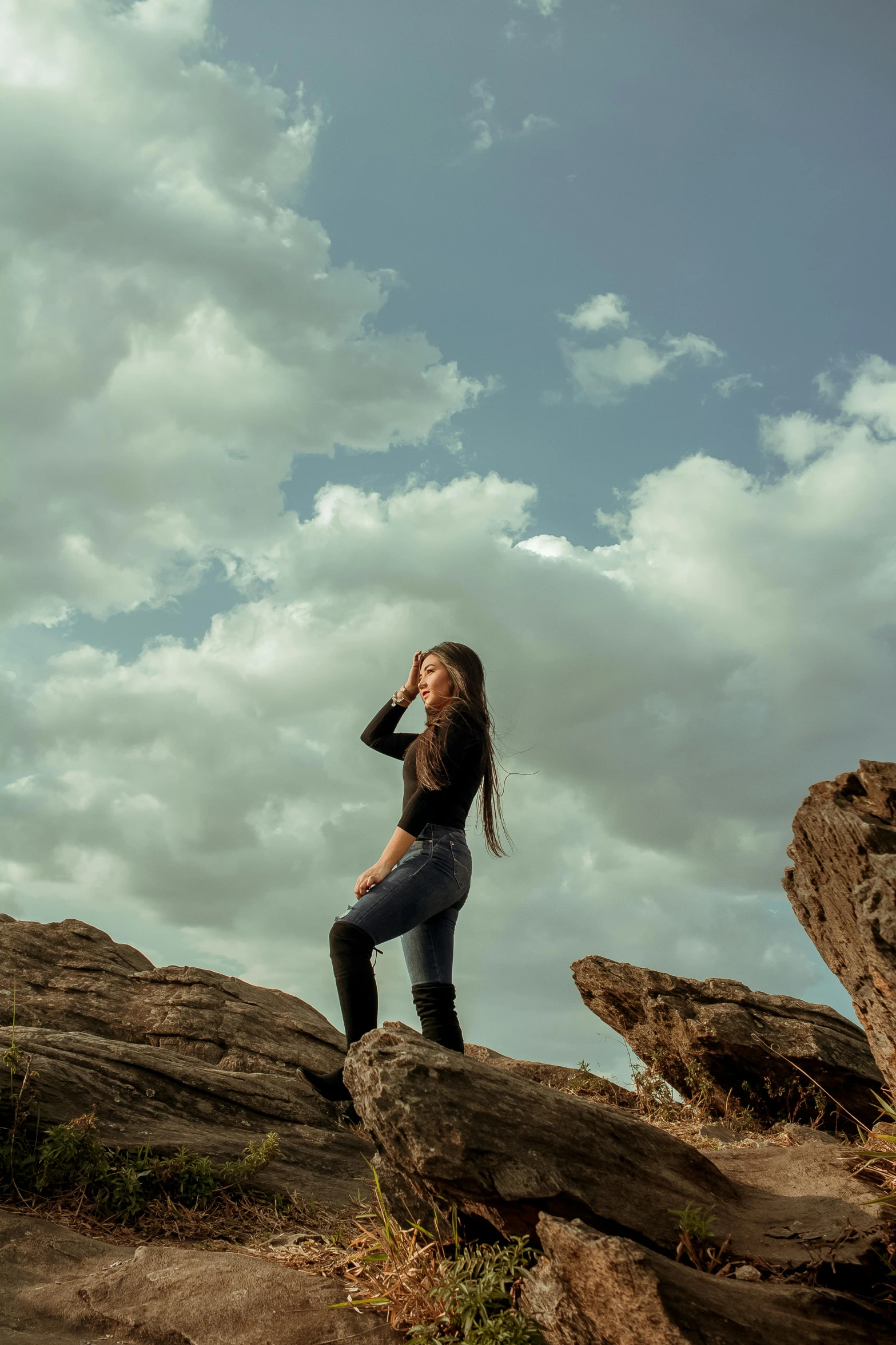 a woman standing on top of a large rock, trending on pexels, girl clouds, side portrait rugged girl, “ iron bark, profile pic