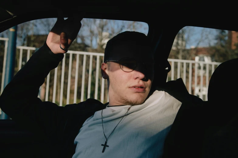 a man sitting in the back seat of a car, an album cover, by Attila Meszlenyi, pexels contest winner, wearing a baseball cap, christian saint, promotional image, in an american suburb