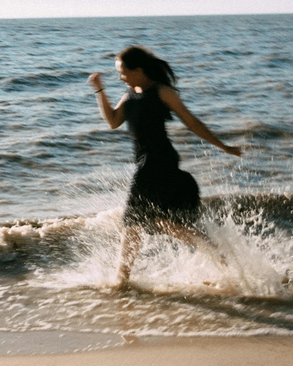 a woman running through the water on a beach, inspired by Annie Leibovitz, unsplash, renaissance, vhs footage still, wearing a black dress, low quality grainy, phoebe tonkin