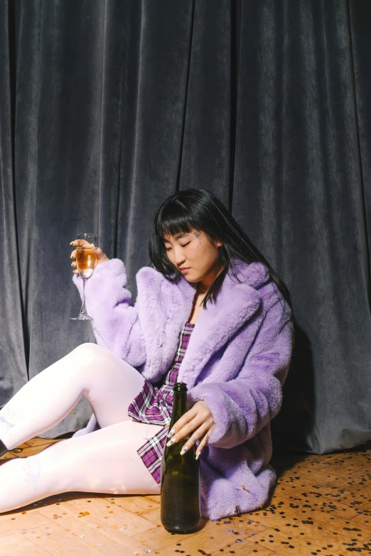 a woman sitting on the floor next to a bottle of wine, an album cover, trending on pexels, realism, purple jacket, asian descent, furry shot, drinking champagne