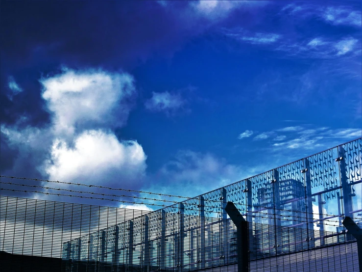 a close up of a fence with a sky in the background, inspired by Richard Wilson, pexels contest winner, modernism, buildings made out of glass, prison complex, under blue clouds, shot on hasselblad