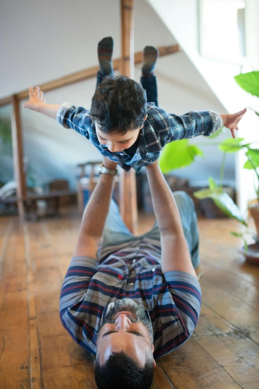 a man laying on the floor with a child on his back, inspired by The Family Circus, things hanging from ceiling, square, fatherly, thumbnail