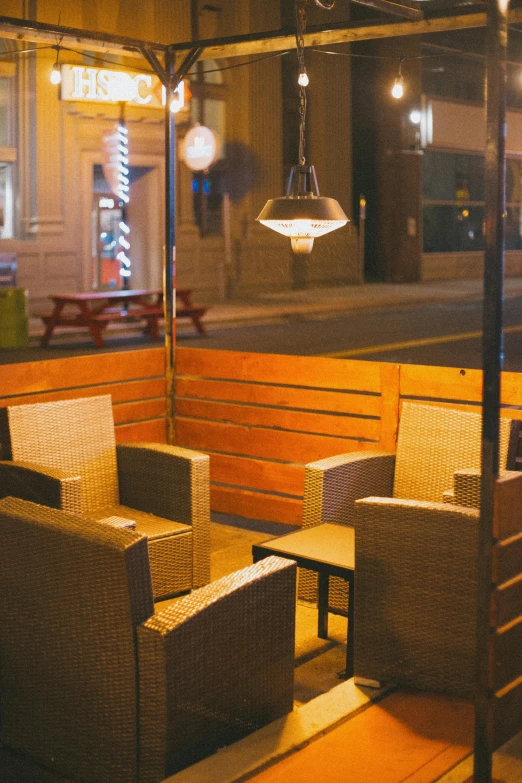 a couple of chairs sitting on top of a wooden bench, warm street lights store front, patio, lounge