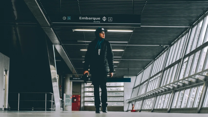 a man standing on a skateboard in a building, black. airports, woman in streetwear, traveling in france, fan favorite