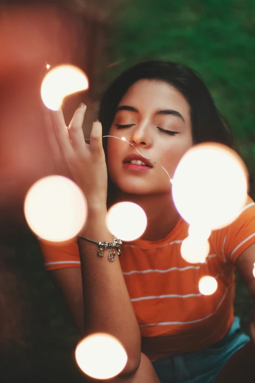 a woman holding a string of lights in front of her face, trending on pexels, magic realism, handsome girl, relaxing, dua lipa, orange hue