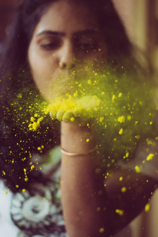 a woman blowing yellow powder on her face, hindu aesthetic, splatter, lo fi colors, dust molecules