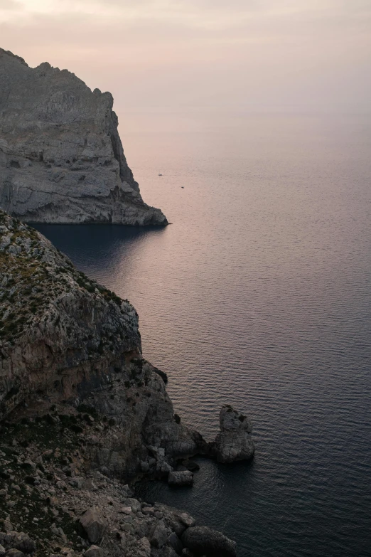 a man standing on top of a cliff next to a body of water, a picture, inspired by Fede Galizia, les nabis, calanque, cliff side at dusk, “ aerial view of a mountain, today\'s featured photograph 4k