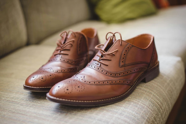 a pair of brown shoes sitting on top of a couch, dapper, detailed features, most popular, laces