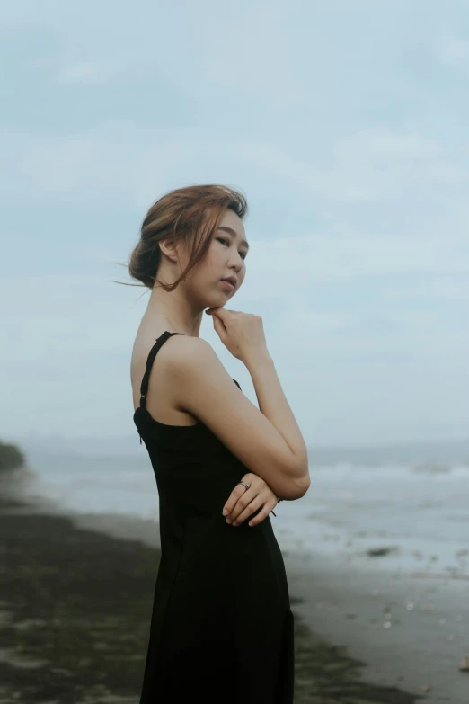 a woman standing on a beach next to the ocean, inspired by Ruth Jên, unsplash, realism, japanese model, wearing a dark dress, indonesia, sleeveless