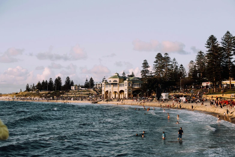 a group of people standing on top of a beach next to the ocean, an victorian city, people swimming, unsplash photography, caulfield