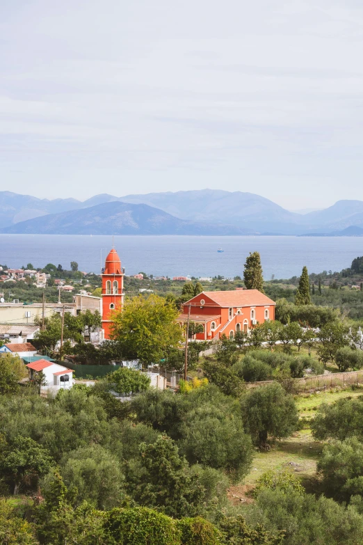 a view of a town from the top of a hill, red building, island in the background, lush surroundings, greek setting