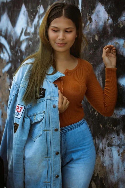 a woman standing in front of a graffiti covered wall, an album cover, trending on pexels, wearing a jeans jackets, she has long orange brown hair, 15081959 21121991 01012000 4k, 2 4 year old female model