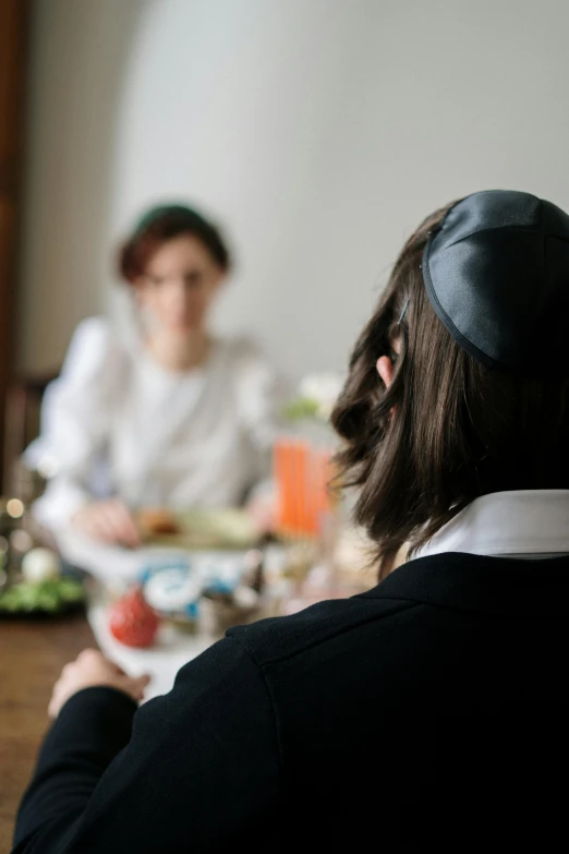 a woman sitting at a table with a plate of food in front of her, by Elias Goldberg, pexels, renaissance, jewish young man with glasses, shot from the back, medium shot of two characters, square