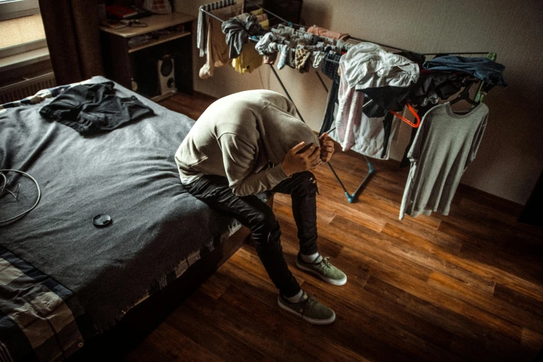 a person bending over on a bed in a room, pexels contest winner, happening, worn out clothes, he is sad, outlive streetwear collection, recovering from pain