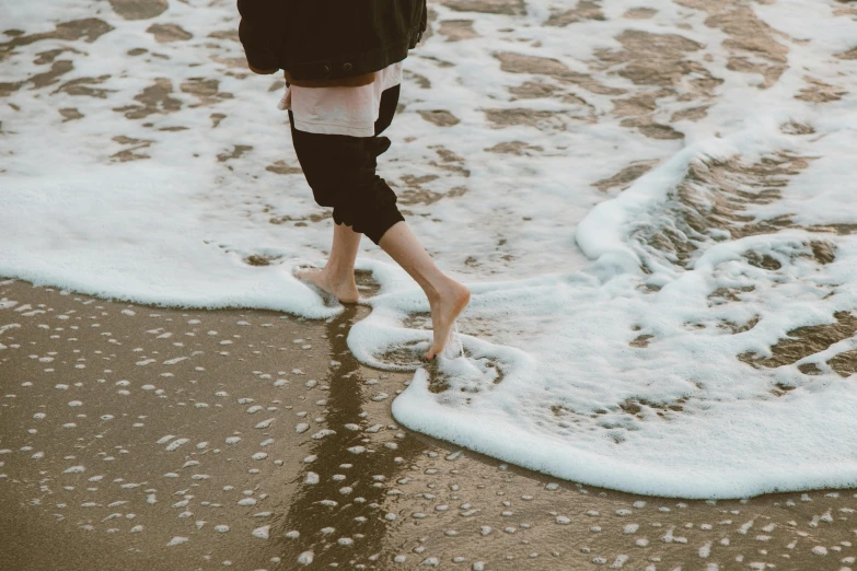 a person walking on a beach next to the ocean, trending on unsplash, happening, wet feet in water, sea of milk, bare thighs, foamy waves