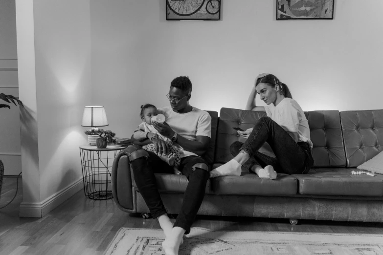 a couple of people that are sitting on a couch, a black and white photo, with a kid, lesbians, reading new book, riyahd cassiem