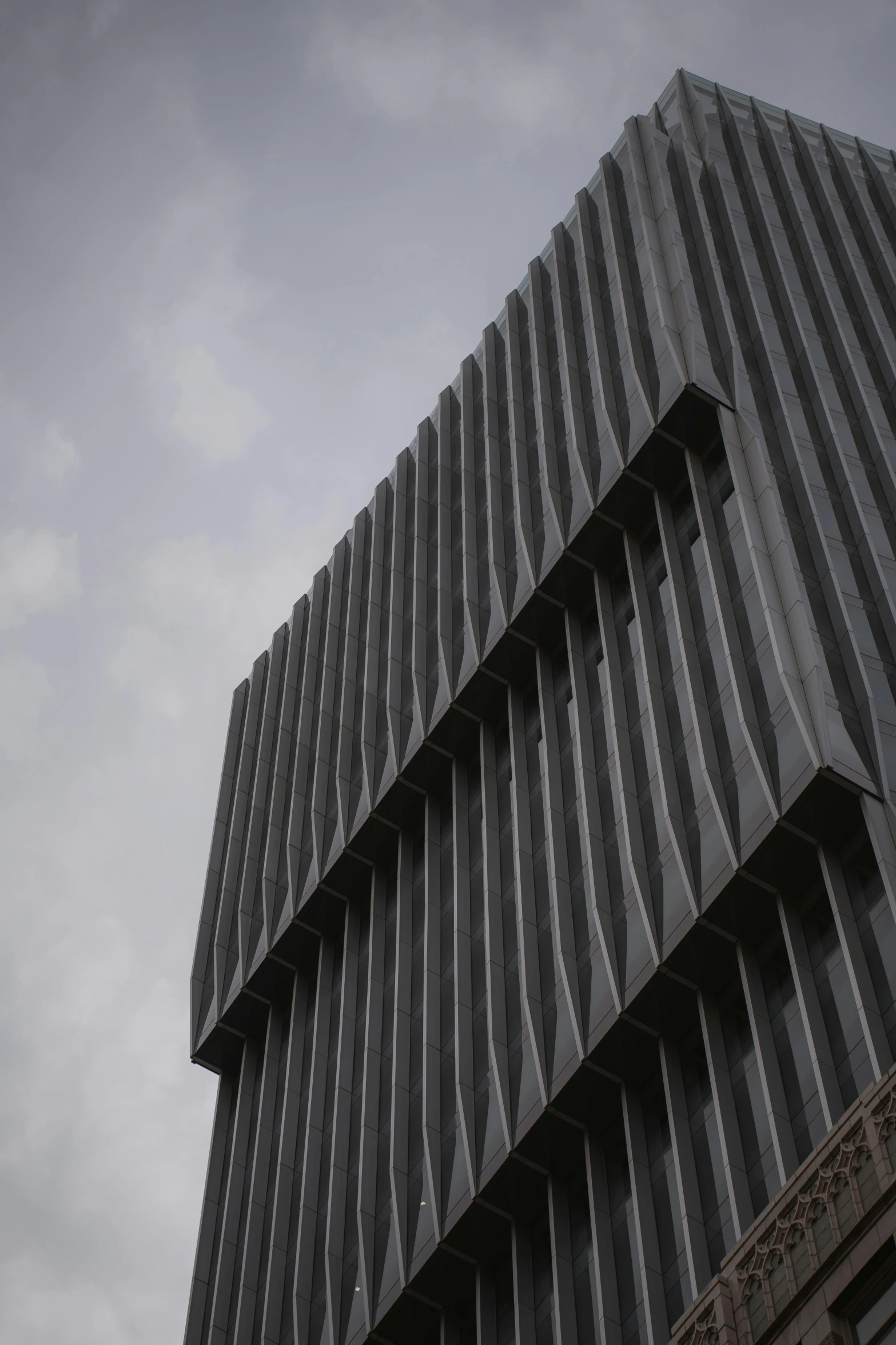 a black and white photo of a tall building, inspired by David Chipperfield, unsplash, black vertical slatted timber, close up shot from the side, grey sky, sculptural