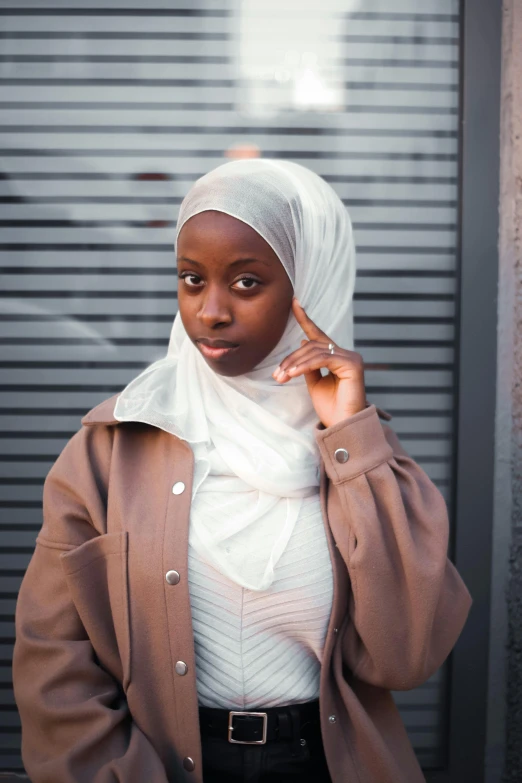 a woman in a hijab talking on a cell phone, an album cover, trending on unsplash, ( brown skin ), in white turtleneck shirt, looking serious, wearing jacket