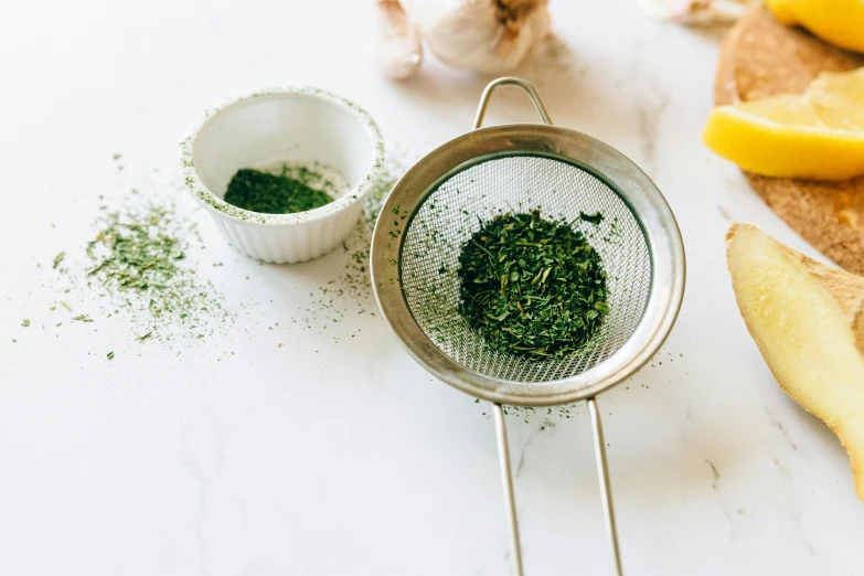 a metal strainer filled with herbs next to sliced lemons, trending on unsplash, scales with magic powder, plume of seaweed, on a white table, green