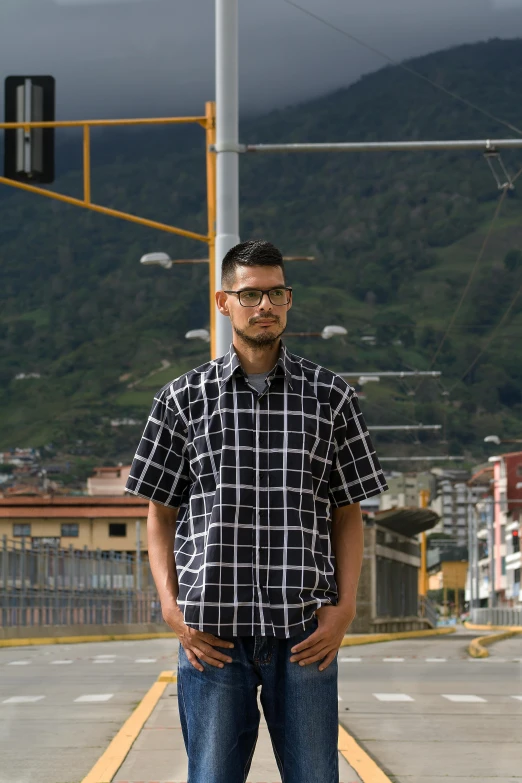 a man standing in the middle of a street, inspired by Eddie Mendoza, hurufiyya, wearing a plaid shirt, with mountains as background, square lines, colombian