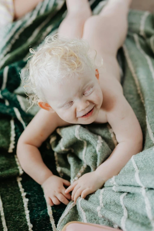 a baby laying on top of a green blanket, unsplash, fine art, cheeky smile, albino white pale skin, 4yr old, over his shoulder