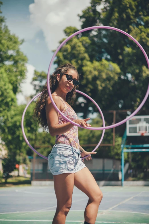 a woman standing on top of a tennis court holding a hula hoop, pexels contest winner, girl wearing round glasses, purple and pink leather garments, wearing a camisole and shorts, at a park