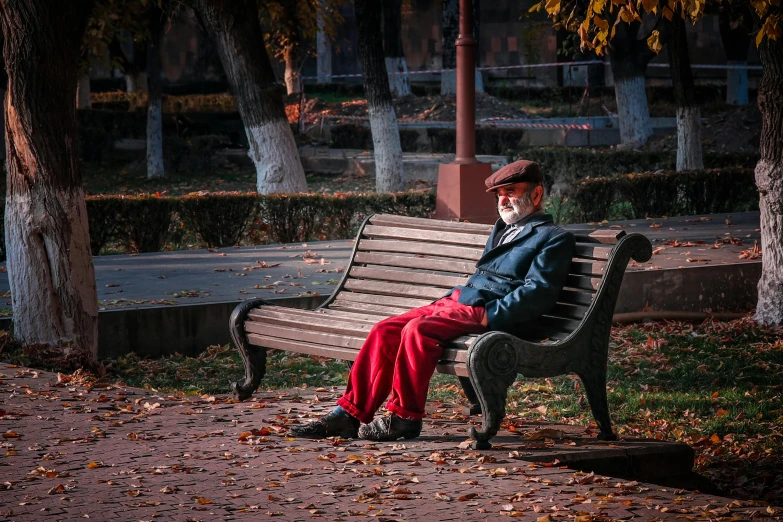 a man sitting on top of a wooden bench, by irakli nadar, pexels contest winner, socialist realism, he has a red hat, autumn season, grumpy [ old ], parks and public space