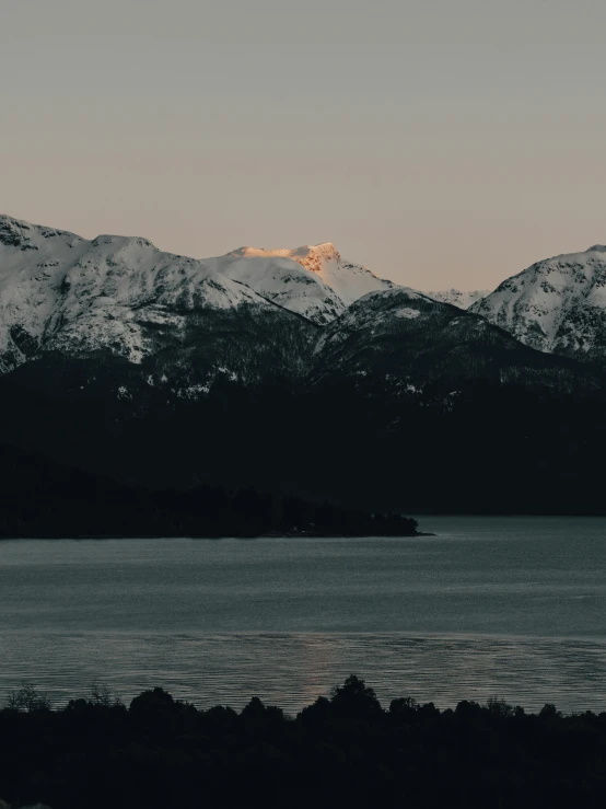 a large body of water surrounded by snow covered mountains, an album cover, unsplash contest winner, filtered evening light, patagonian, whistler, low quality photo