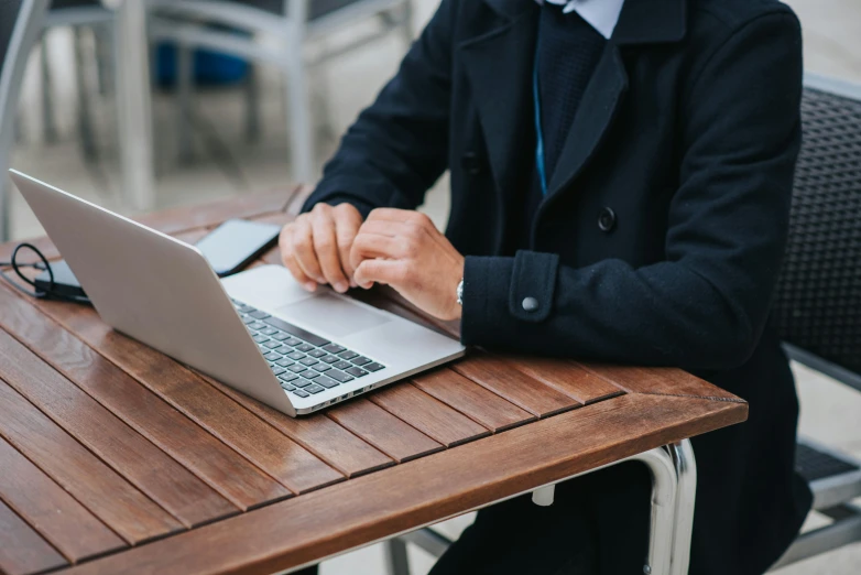 a man sitting at a table using a laptop computer, trending on unsplash, wearing a black blazer, lachlan bailey, sit on a bench, fully covered