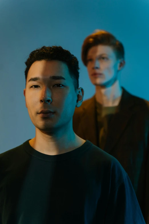 two men standing next to each other in front of a blue background, an album cover, unsplash, lee madgwick & liam wong, androids, in front of a black background, cheekbones