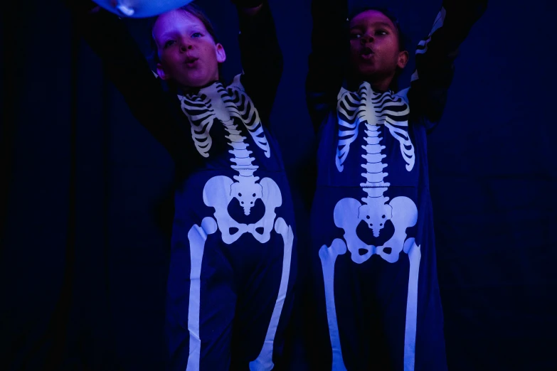 a couple of people that are standing in the dark, by Helen Stevenson, unsplash, process art, cute skeleton, dark blue leotard costume, boys, schools