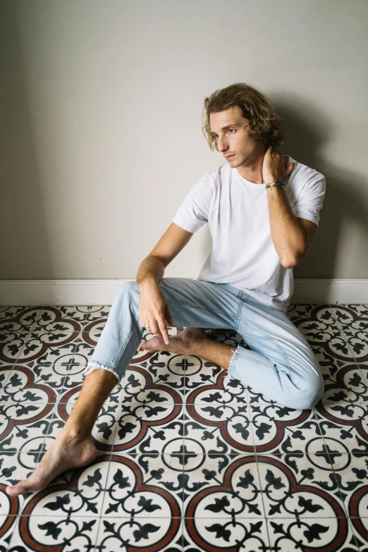 a man sitting on the floor in a room, inspired by Anthony Devas, unsplash contest winner, renaissance, wavy hair spread out, white shirt and jeans, tiles, profile image