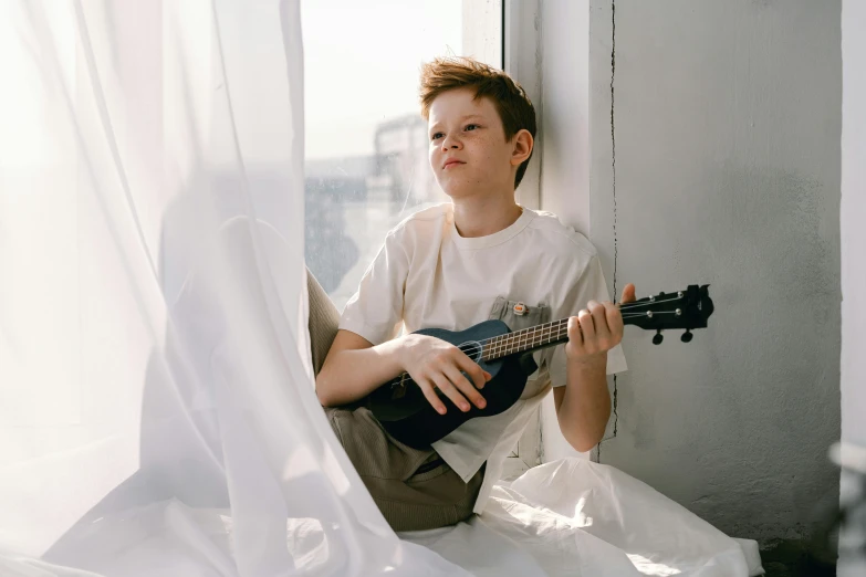 a boy sitting on a window sill playing a guitar, by Julia Pishtar, pexels contest winner, wearing a light shirt, greta thunberg, ukulele, background image