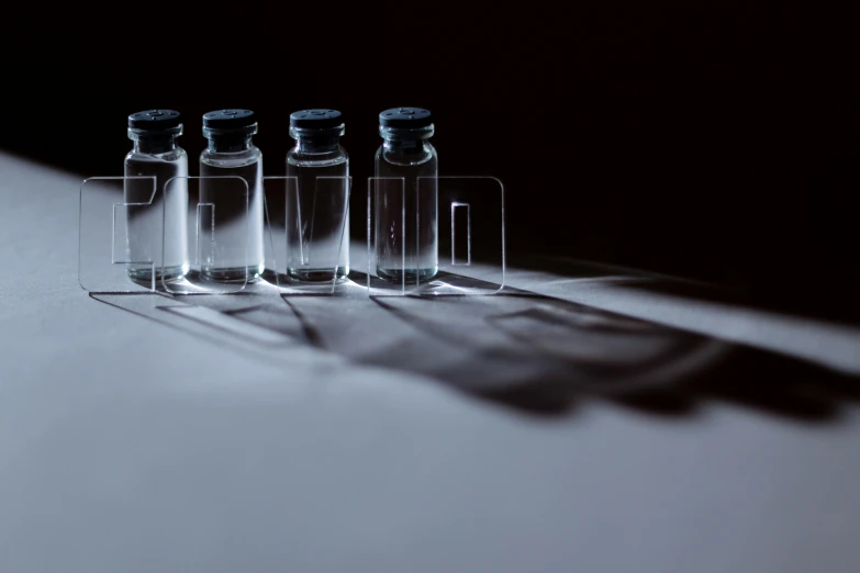 a row of small bottles sitting on top of a table, a hologram, by Adam Marczyński, unsplash, hyperrealism, shadow play, medical photography, shadows of the past, enveloped in ghosts