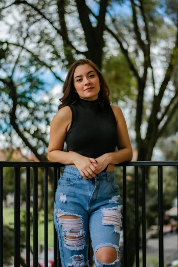 a woman standing on a railing in a black top and ripped jeans, a portrait, by Robbie Trevino, avatar image, college, hispanic, sleeveless
