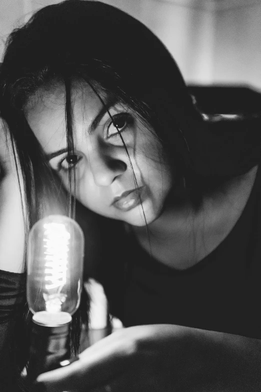 a black and white photo of a woman holding a microphone, a black and white photo, inspired by irakli nadar, pexels contest winner, holding up a night lamp, looking sad, holding electricity, led