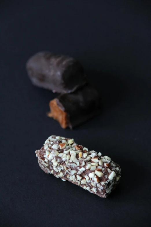 two chocolate bars sitting next to each other on a black surface, by Jessie Algie, hurufiyya, cannonballs, miniatures, luscious with sesame seeds, thumbnail