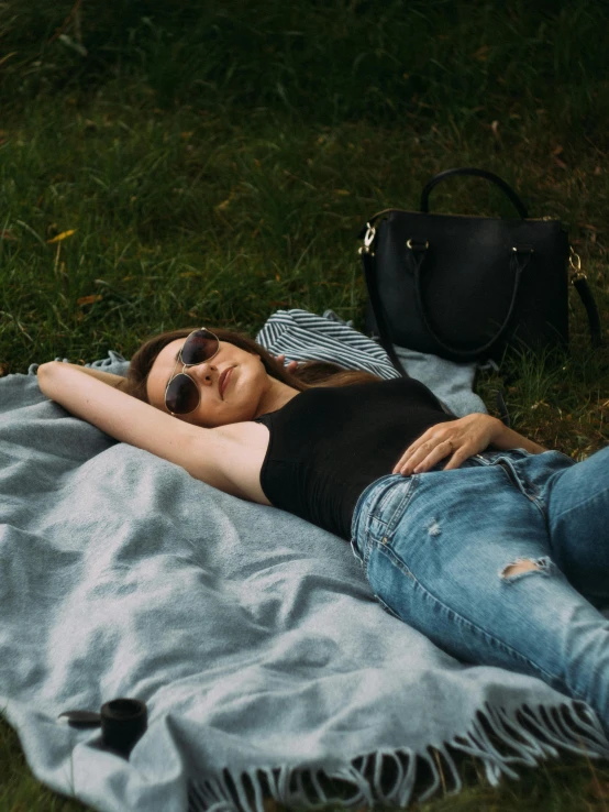 a woman laying on a blanket in the grass, inspired by Elsa Bleda, pexels contest winner, happening, black leather slim clothes, bag over the waist, jeans and t shirt, wearing black camisole outfit