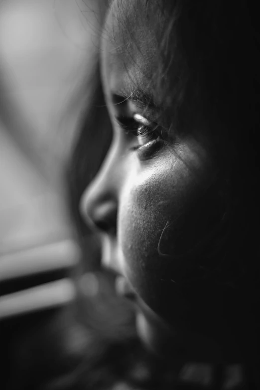 a close up of a child looking out a window, a black and white photo, by Adam Marczyński, pexels contest winner, woman's face looking off camera, close - up of face, abused, closeup shot of face